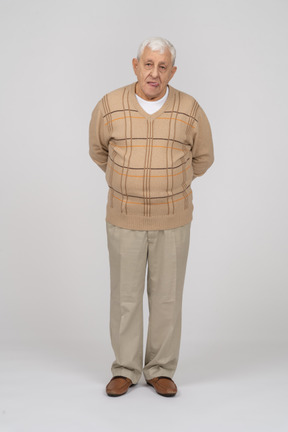 Vue de face d'un vieil homme en vêtements décontractés debout avec les mains derrière le dos et regardant la caméra