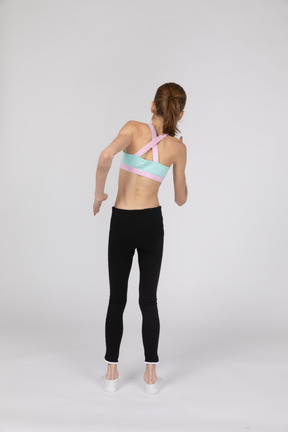 Back view of a teen girl in sportswear leaning aside while standing like a robot
