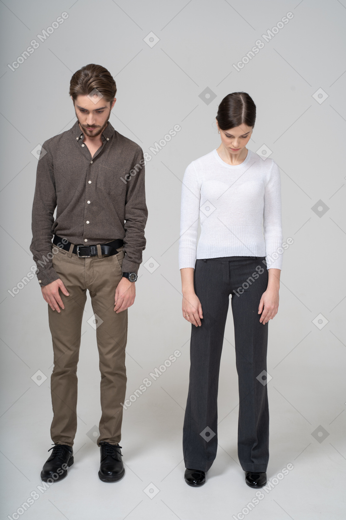 Vista frontal de una joven pareja en ropa de oficina mirando hacia abajo