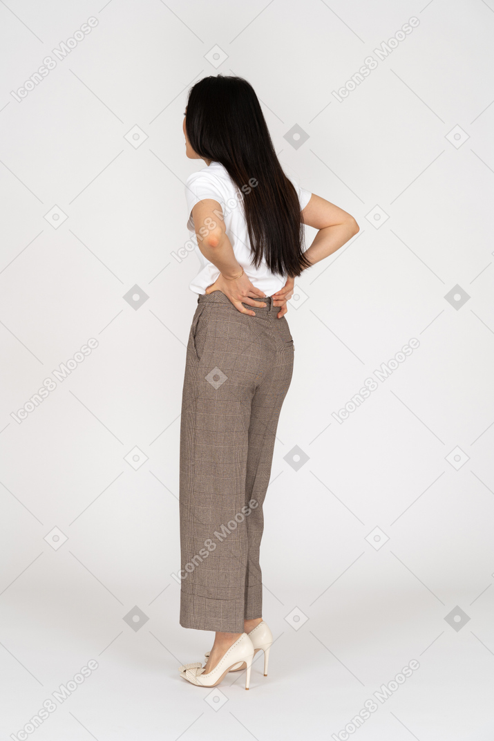 一位年轻的女士，穿着马裤和t恤抚摸她的背的四分之三后视图
