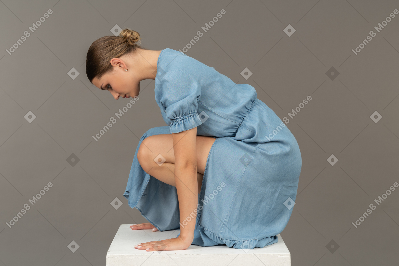 Вид сбоку на молодую женщину, сидящую на корточках на кубе