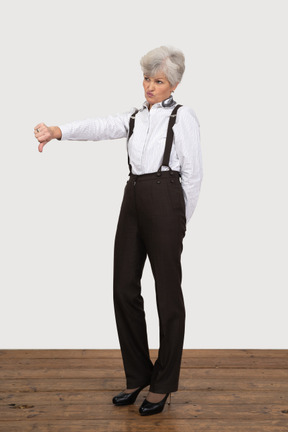 Vista di tre quarti di una vecchia signora in abiti da ufficio mettendo il pollice verso il basso
