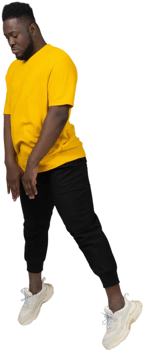 Three-quarter view of a jumping young dark-skinned man in yellow t-shirt looking down