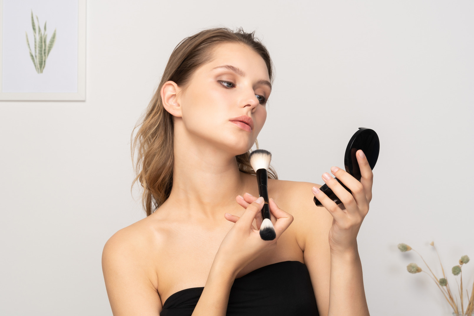 Front view of a young woman applying face powder while holding a mirror
