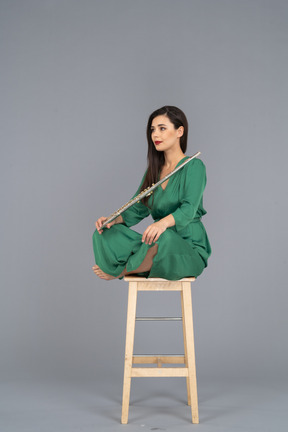 Full-length of a young lady holding the clarinet sitting with her legs crossed on a wooden chair