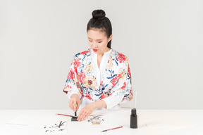 Young woman in a colourful japanese kimono learns calligraphy by drawing a hieroglyph