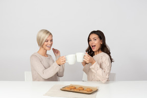 Young women drinking coffee with cookies and laughing