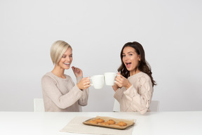 Mujeres jóvenes bebiendo café con galletas y riendo