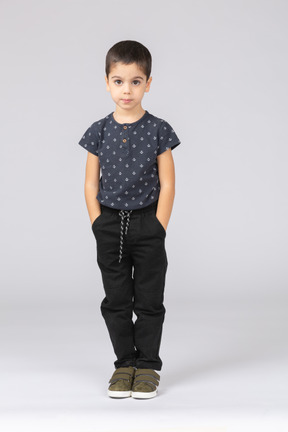 Вид спереди симпатичного мальчика в повседневной одежде, позирующего с руками в карманах и смотрящего в камеру