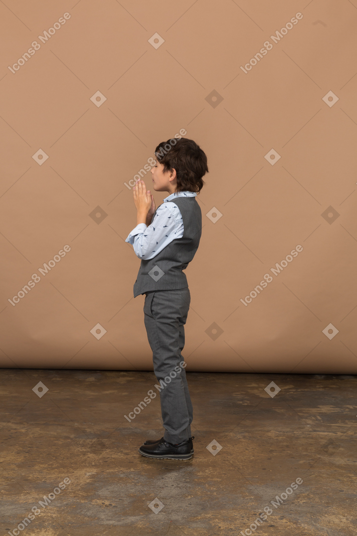 一个穿西装的男孩做祈祷手势的侧视图
