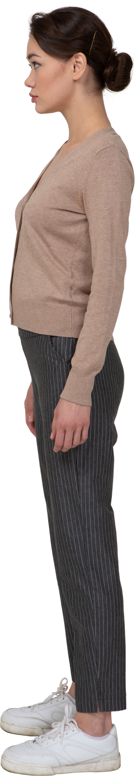 Vista lateral de una señorita parada quieta en jersey y pantalones mirando a un lado