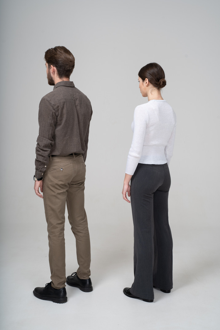 Three-quarter back view of an unrecognizable young couple in office clothing standing still