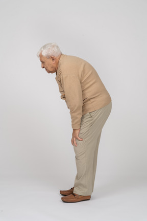 Side view of an old man in casual clothes bending down and touching his hurting knee
