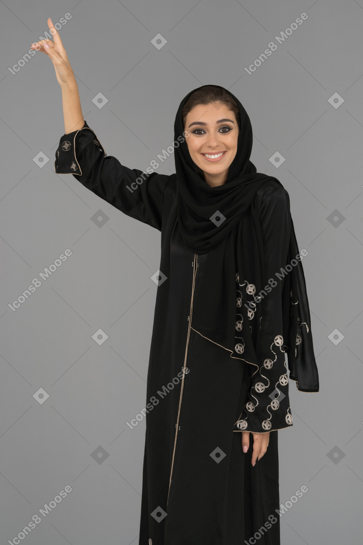 A smiling muslim woman pointing upwards