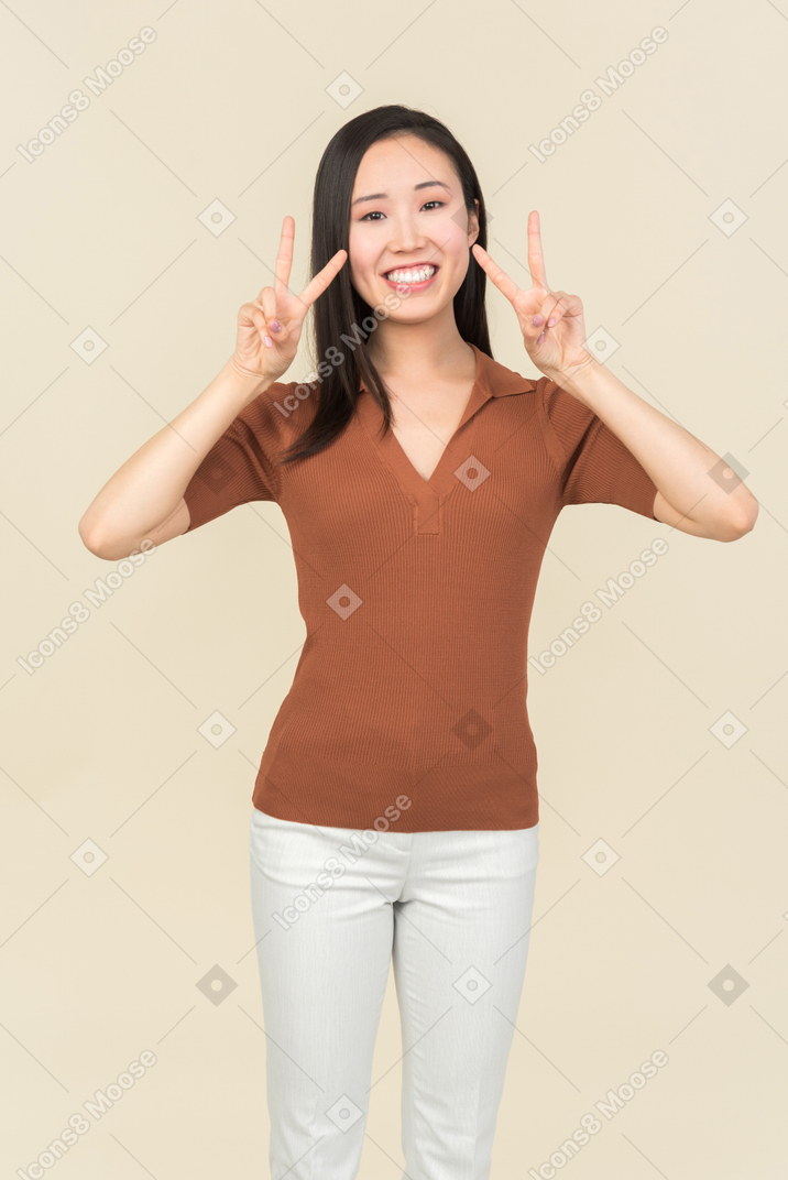Smiling young asian woman showing double victory gestures