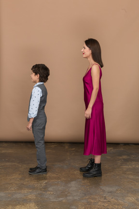 Stylsih woman in red dress and boy in suit vest standing in profile