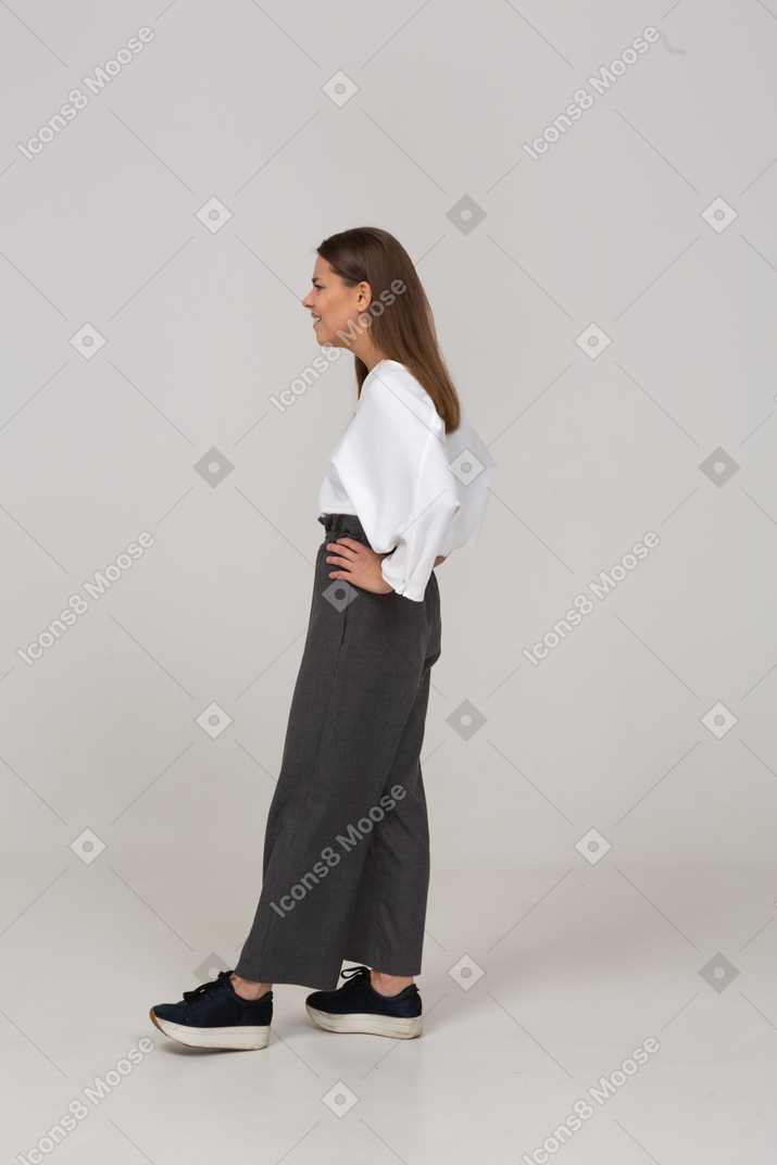 Side view of a confused young lady in office clothing putting hands on hips