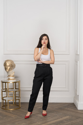 Front view of a young female looking thoughtfully aside while standing by golden greek sculpture