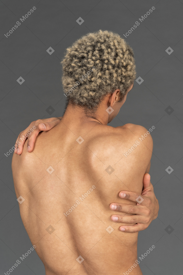 Back view of a shirtless man wrapping his arms around himself