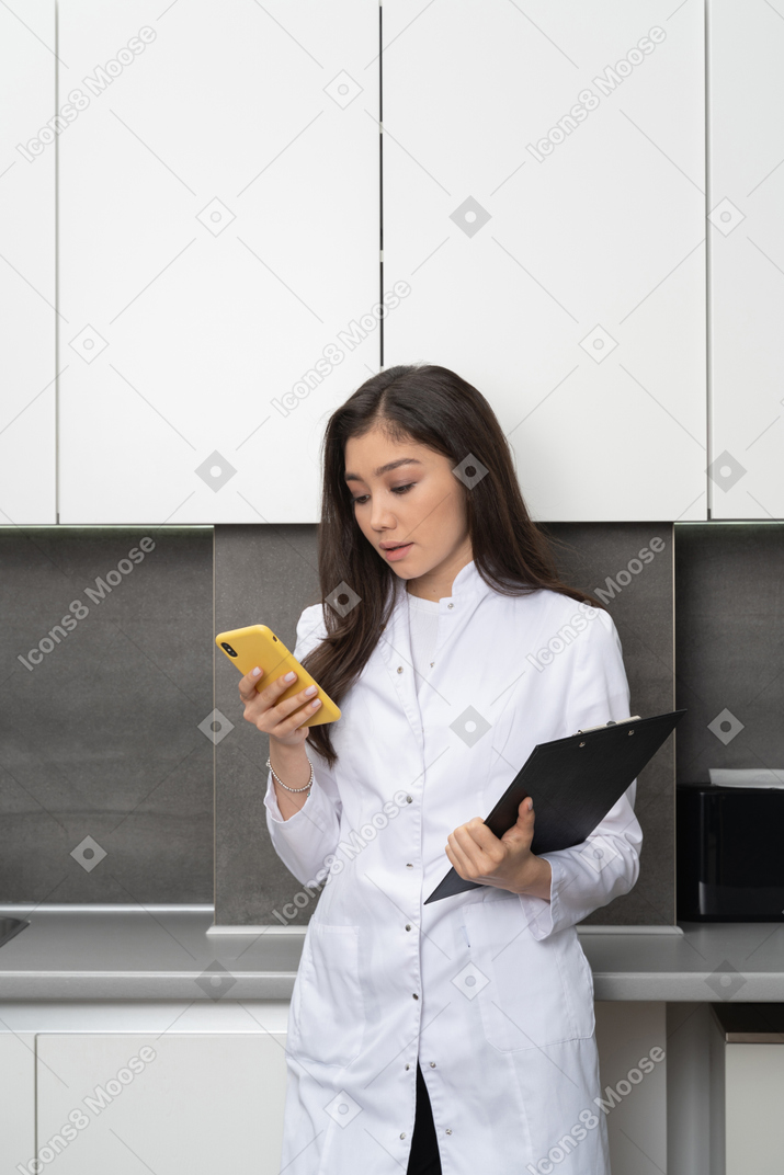 Vista frontal de uma jovem médica segurando seu telefone e um tablet