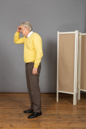 Side view of an old man having a headache while touching his forehead