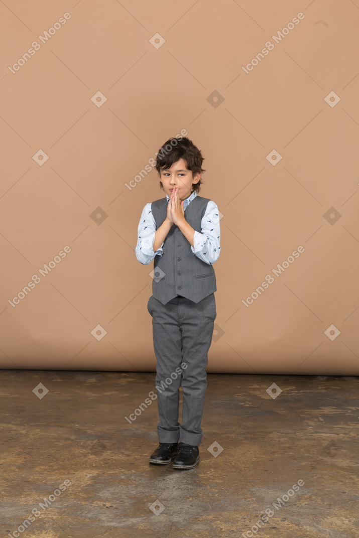 Вид спереди мальчика в сером костюме, делающего молитвенный жест