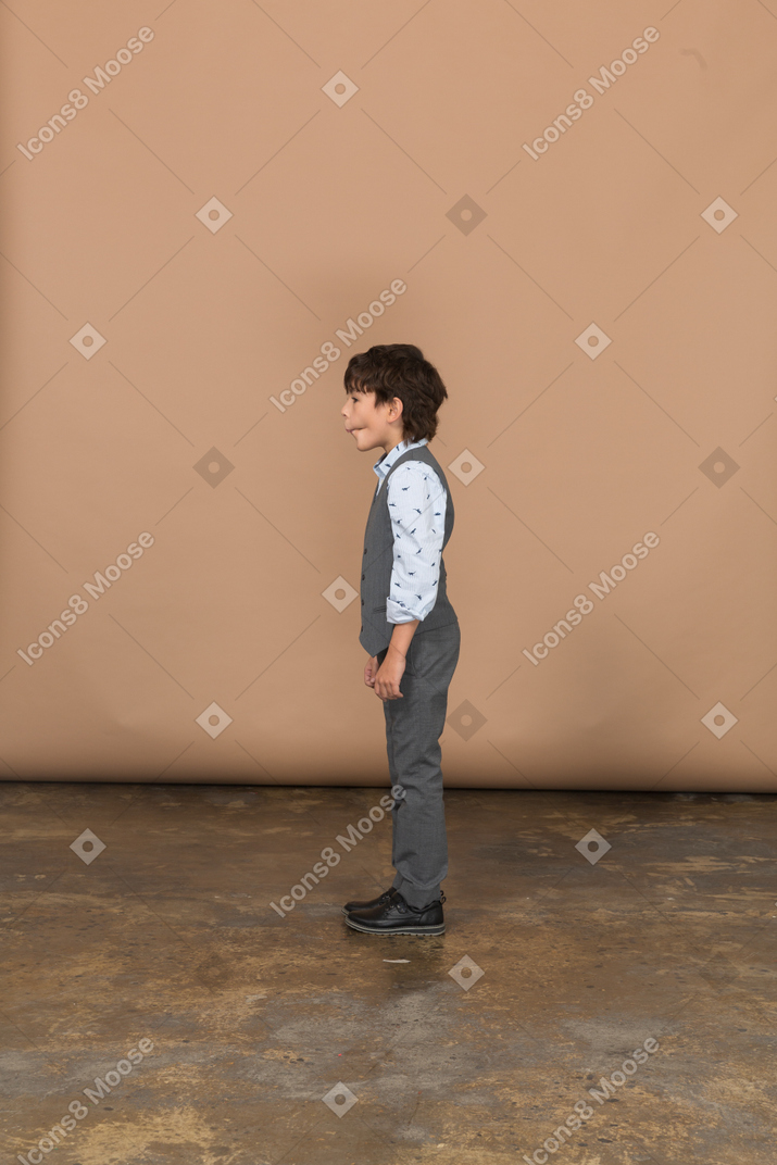 Boy in grey suit standing in profile and making faces