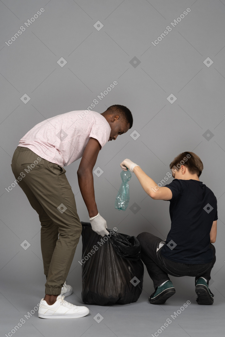 Deux jeunes hommes organisant un sac poubelle noir