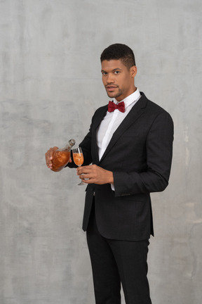 Young man pouring liquid into a glass and looking at camera