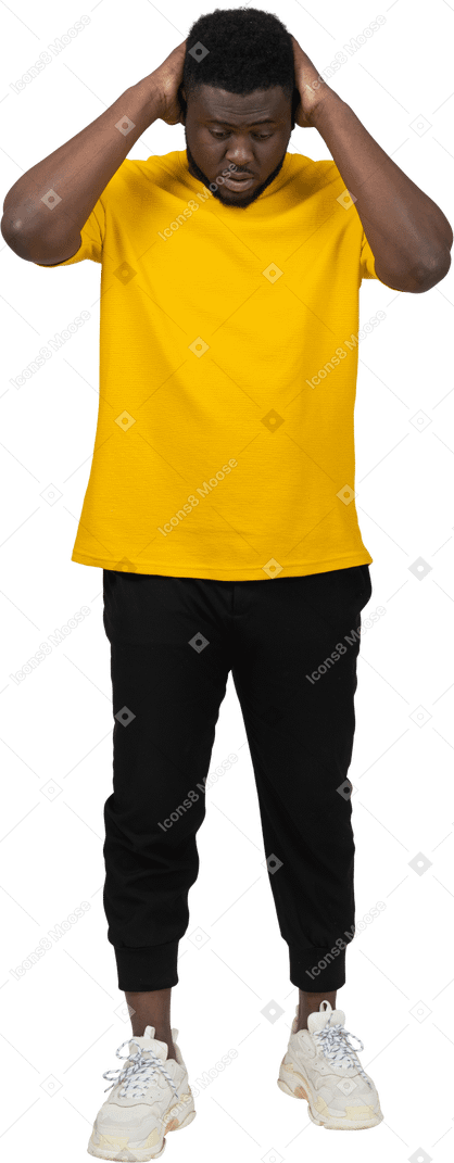 Vista frontal de um jovem de pele escura em uma camiseta amarela tocando a cabeça e olhando para baixo