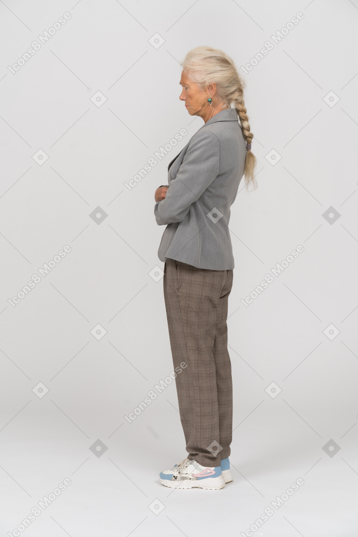Vista lateral de una anciana en traje de pie con los brazos cruzados.