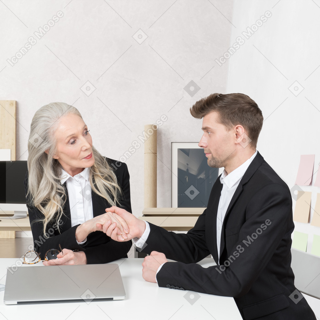 A man and a woman sitting at a table shaking hands