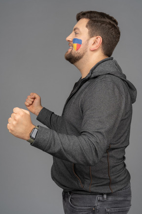 Side view of a satisfied male football fan with colorful face art clenching fists