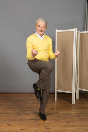 Front view of a happy old man clenching fists and raising his leg