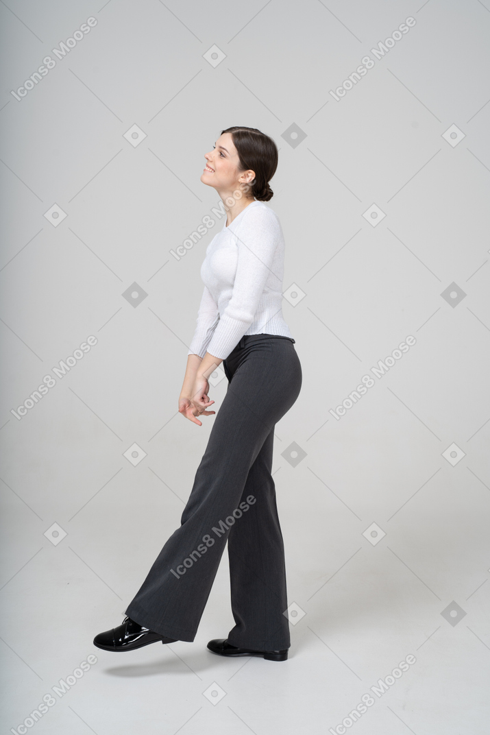 Vista laterale di una donna in pantaloni neri e camicetta bianca in equilibrio su una gamba