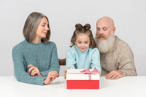 Niña sentada junto a sus abuelos y sosteniendo una caja de regalo.