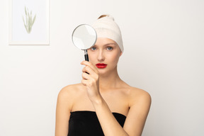 Young woman with bandaged head holding up magnifier