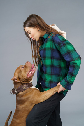 Visão lateral de uma jovem mulher de camisa xadrez beijando seu buldogue marrom