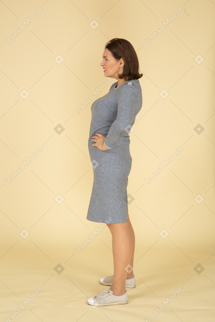 Side view of a woman in grey dress posing with hands on hips