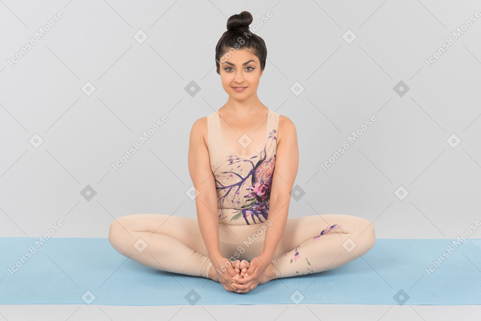 Young indian woman sitting on yoga mat holding toes with her hands