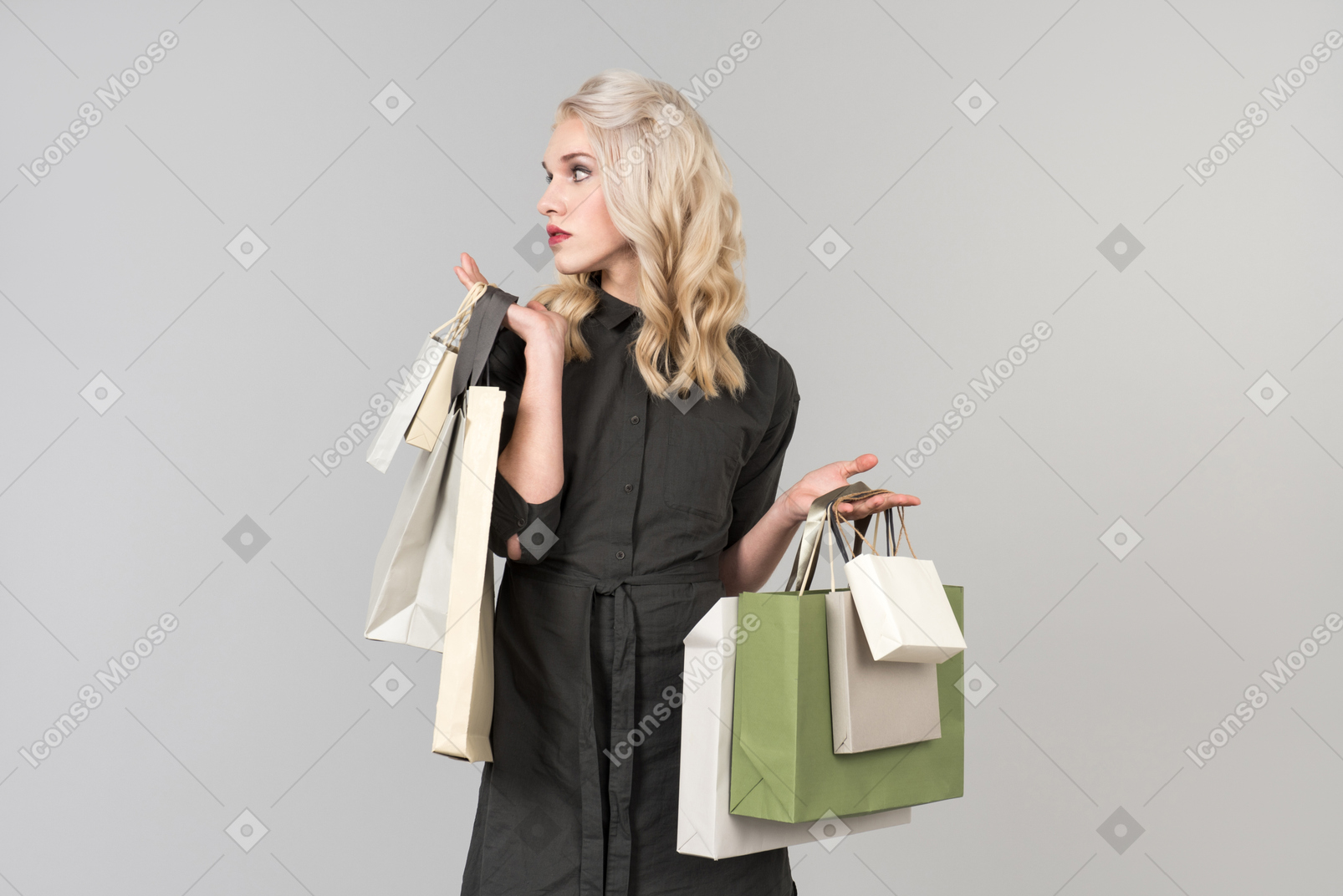 A young beautiful blond-haired person in a black dress holding a bunch of shopping bags in both of their hands