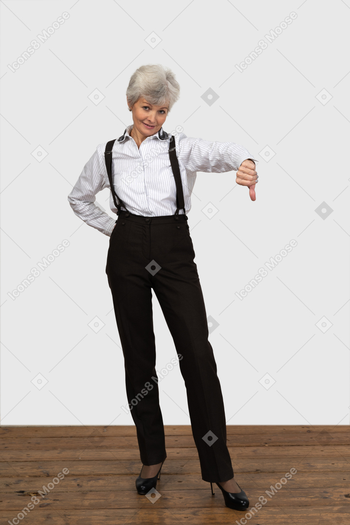 一位老不悦女性在显示拇指向下的办公室衣服的前视图