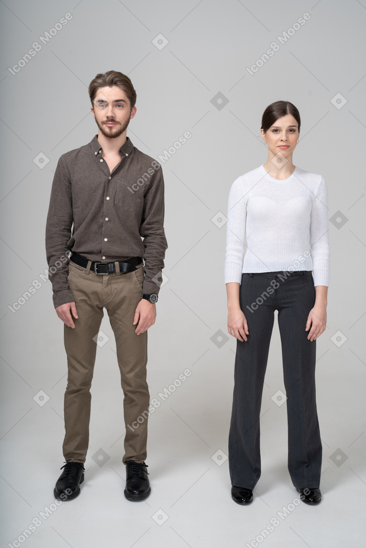 じっと立っているオフィス服を着た若いカップルの正面図