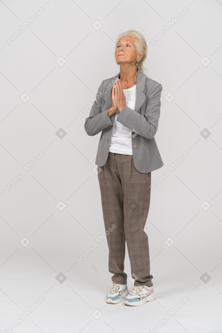 Vista frontal de uma senhora idosa de terno fazendo gestos de oração