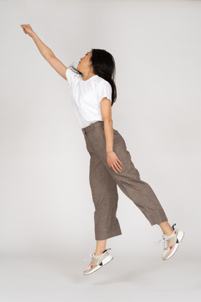 Vue latérale d'une jeune femme sautant en culotte et t-shirt étendant sa main