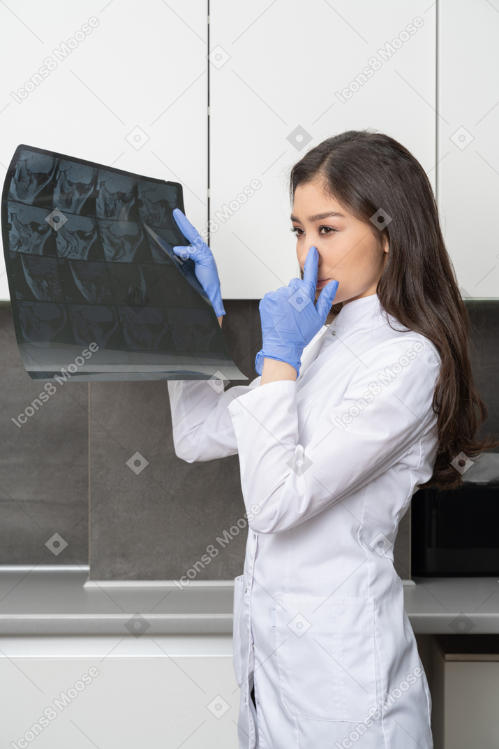 Vista lateral de uma jovem médica segurando uma imagem de raio-x e tocando o nariz