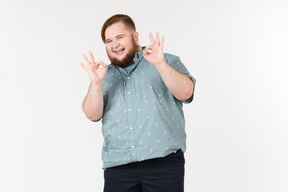 Ridendo giovane uomo in sovrappeso che mostra il gesto ok