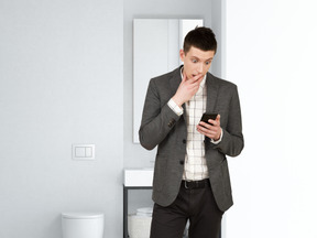 A man standing in a bathroom looking at his cell phone
