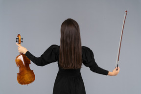 Vista de trás de uma violinista em vestido preto estendendo as mãos