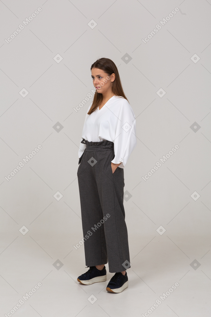 Vista de tres cuartos de una joven en ropa de oficina poniendo las manos en los bolsillos